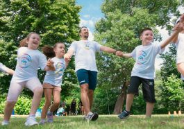 Group of joyful children playing outdoors with an instructor in a sunny park.